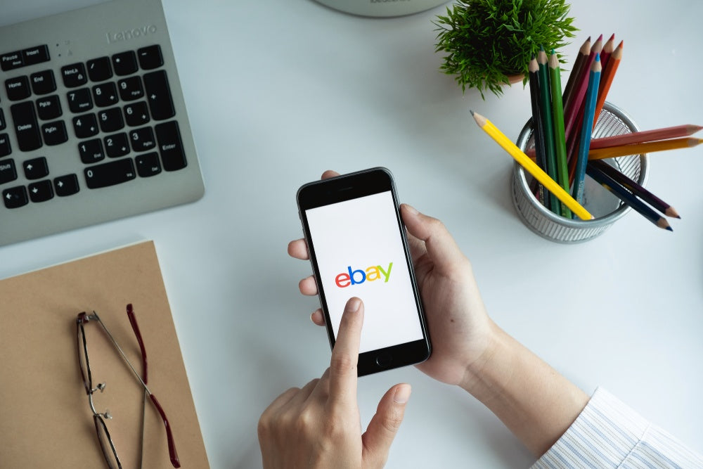 Person holding a cell phone with the eBay logo on the screen