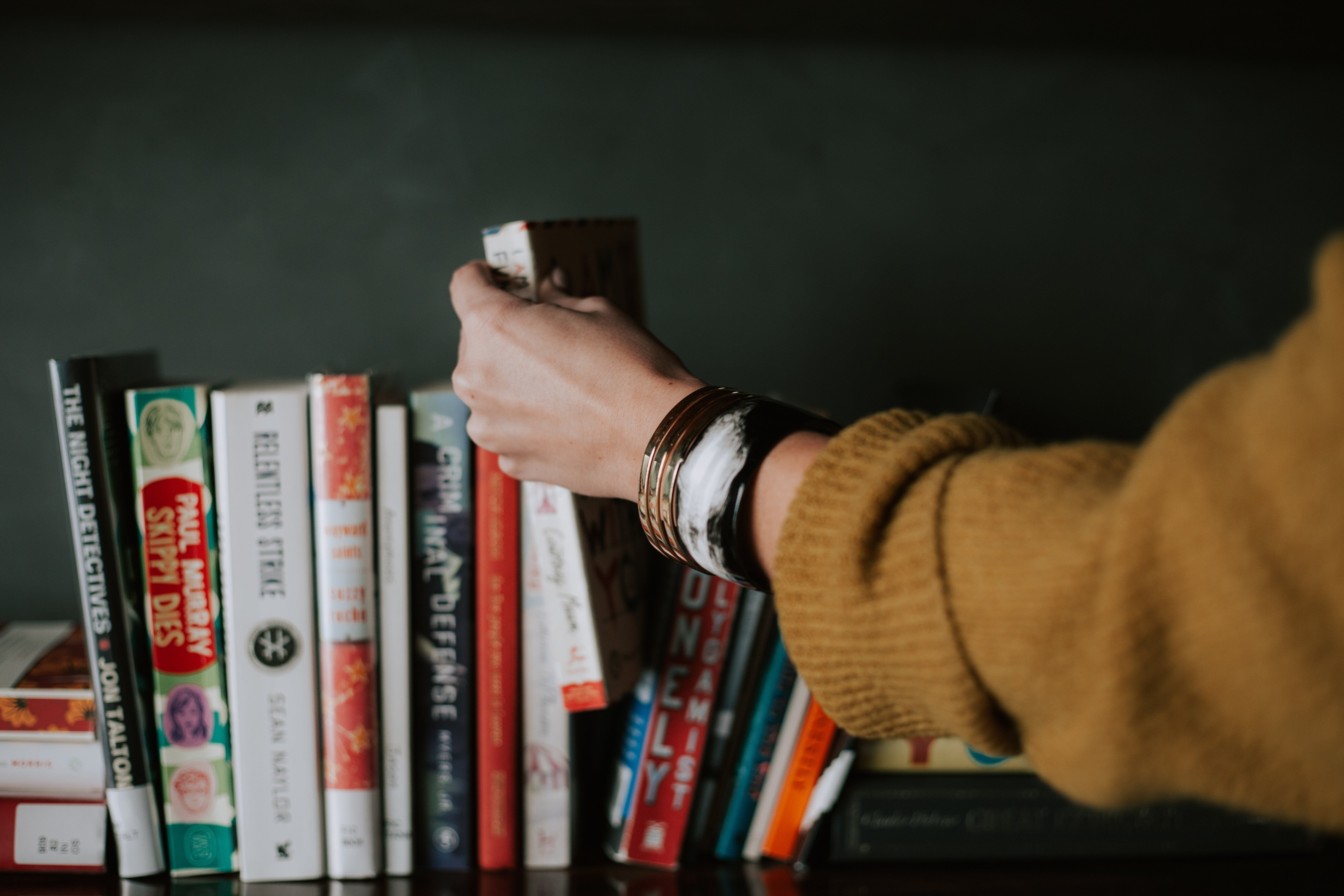 Person picking out a book from a shelf 