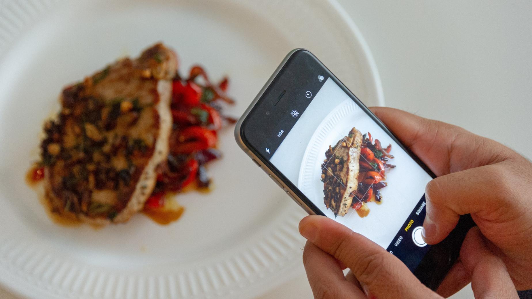 Hands holding a phone to take a picture of a meal: food photography.